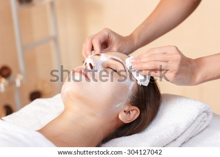 Be beautiful.  Professional spa specialist holding napkin and removing beauty mask from face of nice woman