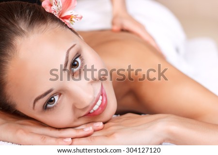 Balance in mind. Close up of cheerful young woman smiling and having massage while lying in spa salon.