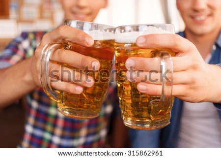 Best beverage. Pleasant upbeat friend holding jugs of beer and going to drink it while relaxing in the pub