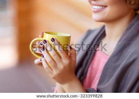 Best way to relive stress. Close up of yellow cup in hands of young girl holding it and reveling in drinking tea