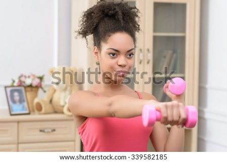 Confidence in mind. Pleasant content young curly girl holding dumbbells and doing morning exercises