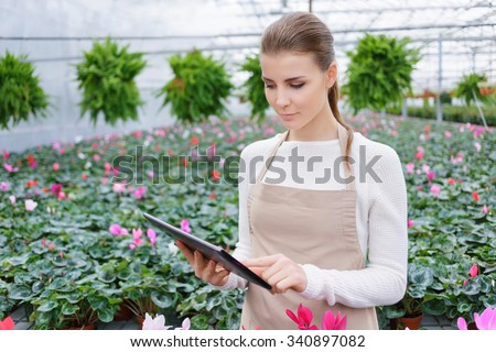 Achieve only best results. Pleasant confident female florist holding laptop and doing her job while standing in  the greenhouse