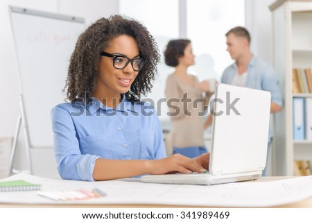 Work with laptop. Young attractive woman is sitting at the desk and working on her laptop while her colleagues are having a coffee break.