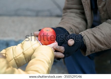 Getting food. Kind little child gives apple to a homeless person.