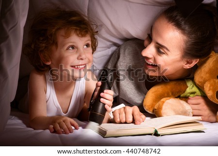 Mother and son reading book under blanket