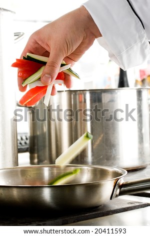 Chef hands add vegetables on a frying pan on professional kitchen