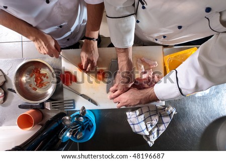 Two chefs cut the tomatoes and chicken in the kitchen