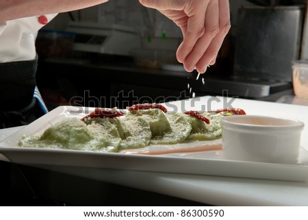 A chief cook masterly preparing delicious green ravioli with pesto sauce at the kitchen decorating raviolli with parmesan