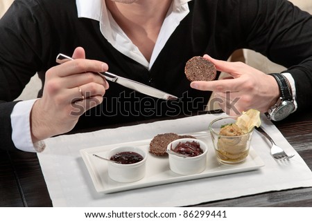 A young man spreading apple jam on a piece of bread, sitting at an elegantly served table in a restaurant