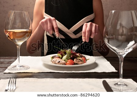 A young woman eating meat salad with stewed and fresh vegetables at an elegantly served table in a restaurant