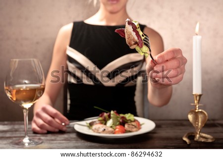 A young woman eating meat salad with stewed and fresh vegetables at an elegantly served table in a restaurant