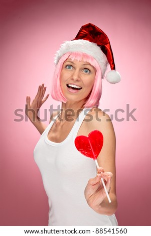 Young female santa in flaunting pink wig with a heart lollypop over red background