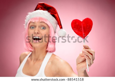 Young female santa in flaunting pink wig with a heart lollypop - focus on candy