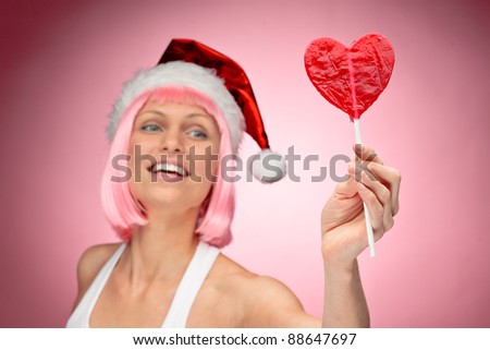 Young female santa in flaunting pink wig with a heart lollypop - focus on candy