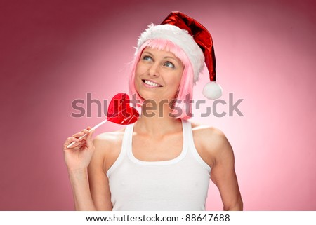 Young female santa in flaunting pink wig with a heart lollypop over red background