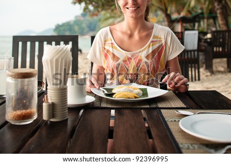 A young and attractive woman having a mango dessert in an outdoor restaurant on a beach