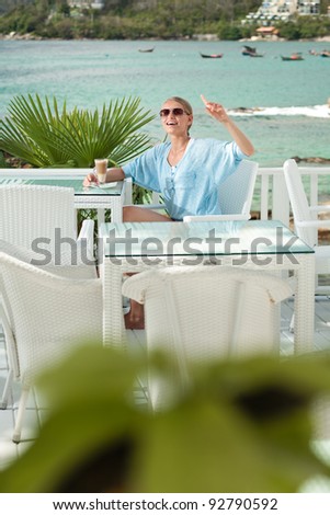 A young and attractive woman call a waiter in an modern outdoor ocean view restaurant