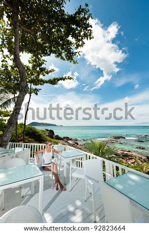 A young and attractive woman having a coffee break in an modern outdoor ocean view restaurant