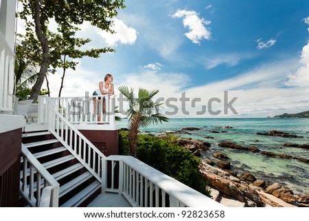 A young and attractive woman stand on a gallery in an modern outdoor ocean view restaurant