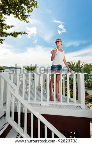 A young and attractive woman stand on a gallery in an modern outdoor ocean view restaurant