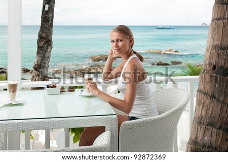 A young and attractive woman sitting on a gallery in an modern outdoor ocean viewpoint restaurant