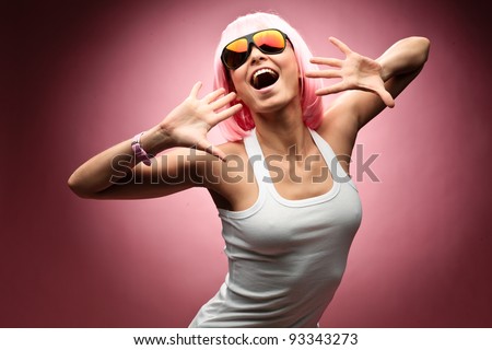 Funny young girl in pink wig and glasses dancing for camera across pink background