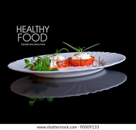 Tomatoes with mozzarella and rosemary on white plate isolated on black background