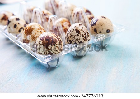 Quail eggs in a transparent plastic container on wooden background