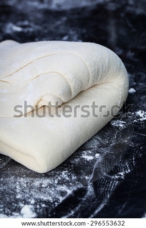 Classic wooden rolling pin with freshly prepared dough and dusting of flour on black background