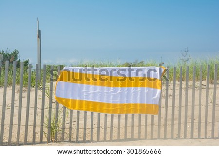 A yellow and white beach towel hanging on a fence drying off at a beach