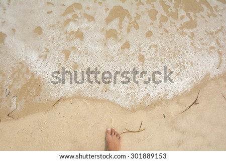 Foot of a woman on a beach and white bubbles created by ocean waves on the seashore