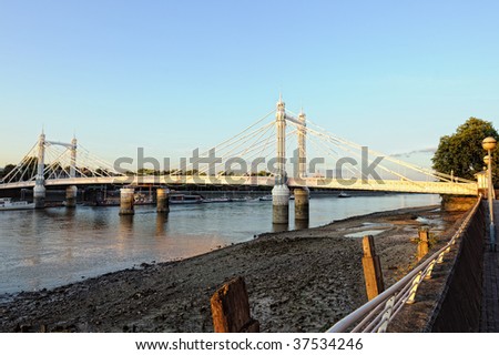 Albert Bridge over the river Thames, London, England, UK, Europe, at low tide, dusk.  A toolbooth is just visble on the extreme right