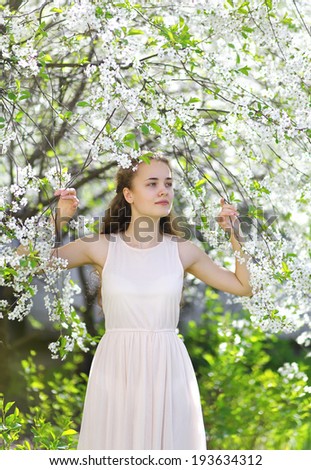 Cute girl in white dress in the blooming garden, looking to the side, clear day