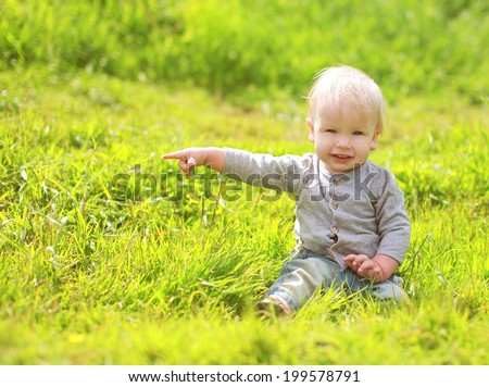 Cute baby sitting on the grass, shows gesture of hand toward