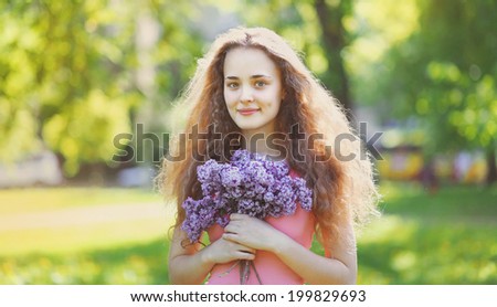 Lovely curly girl with a bouquet of lilacs on a sunny summer day, nice smile, good open look