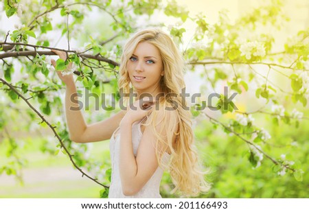 Pretty blonde girl with long hair in floral garden, sunny warm day