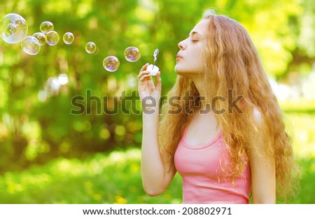Pretty curly girl blowing soap bubbles having fun outdoors in summer day