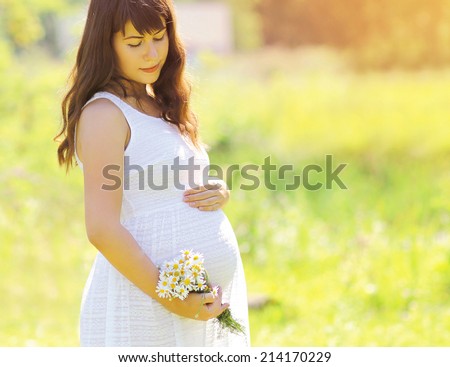 Pregnant lovely woman in white dress and wildflowers in sunny summer day