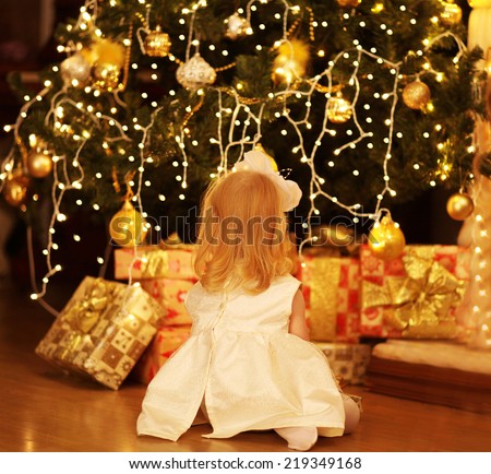 Christmas, magic, people concept - happy baby dreams near christmas tree with gifts