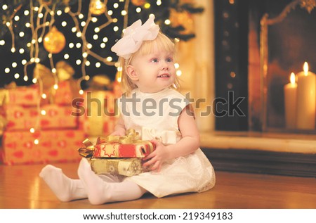 Christmas, magic, people concept - happy baby with gift near christmas tree and fireplace