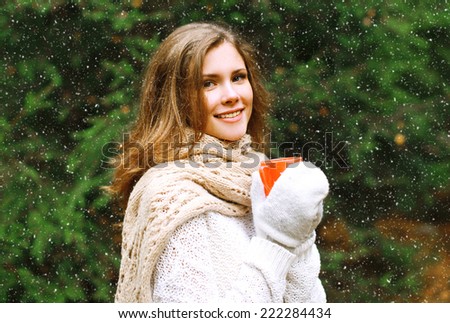 Christmas and people concept - happy cozy young girl with mug outdoors near christmas tree