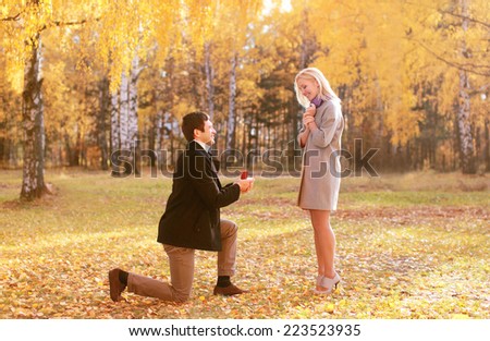 Love, couple, relationship and engagement concept - kneeled man proposing to a woman in the autumn park