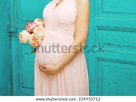 Pregnancy, motherhood and happy future mother concept - pregnant woman in dress with bouquet flowers against colorful wall