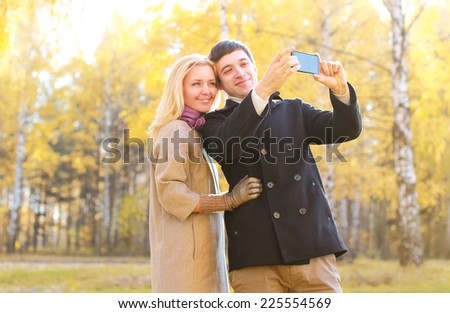 Love, relationship, season, technology and people concept - happy smiling couple in love making selfie in autumn park