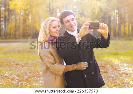 Love, relationship, technology and people concept - happy smiling couple in love making selfie outdoors in autumn park