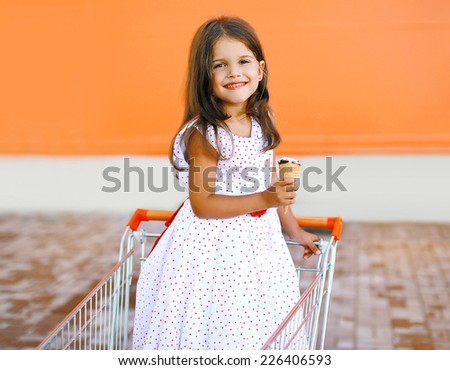 Happy smiling little girl in shopping cart with tasty ice cream outdoors