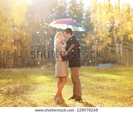 Autumn, love, relationship and people concept - happy kissing couple in love outdoors in autumn park, leafs fall