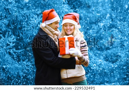 Christmas and people concept - happy man giving a box gift to a woman in winter snowy day