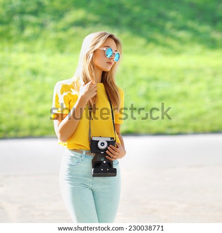 Summer, fashion and people concept - stylish pretty modern girl in sunglasses with retro vintage camera posing in city, street fashion
