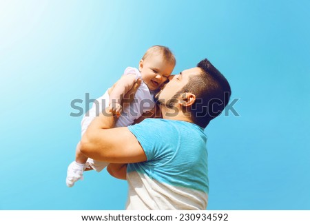 Lifestyle family photo happy father kissing baby outdoors against on summer sunny blue sky